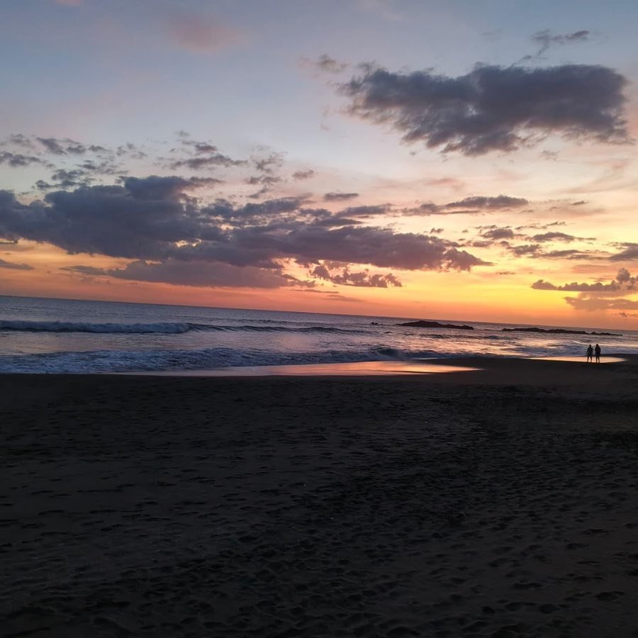 Atardecer sobre el Pacífico en El Tránsito, con nubes teñidas de naranja y la orilla mojada.