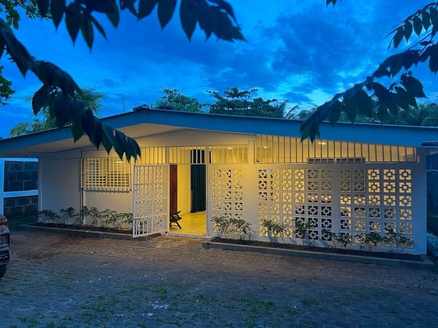 Fachada de la casa iluminada al anochecer entre hojas de árboles.