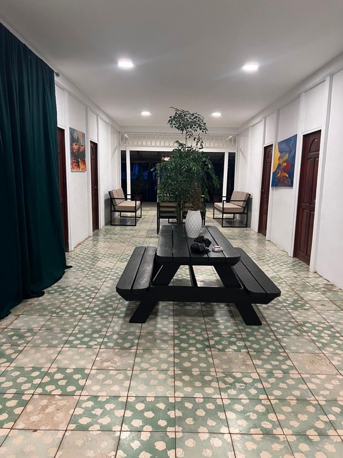 Corredor interior de la casa con mesa larga de madera, plantas y piso de mosaico verde.